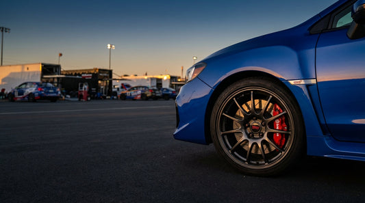 A close-up of a red Brembo brake caliper and slotted rotor installed on a Subaru WRX STI, showcasing a performance brake upgrade.