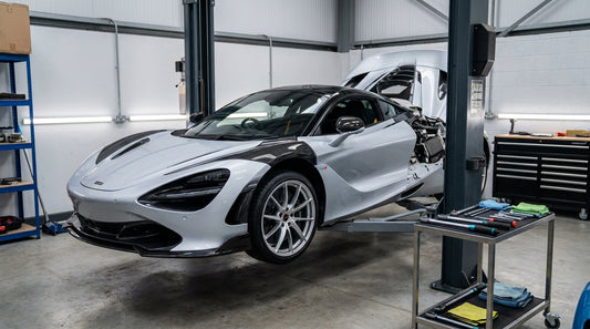McLaren 720S in a clean workshop during carbon kit fitment, front three-quarter on a hoist
