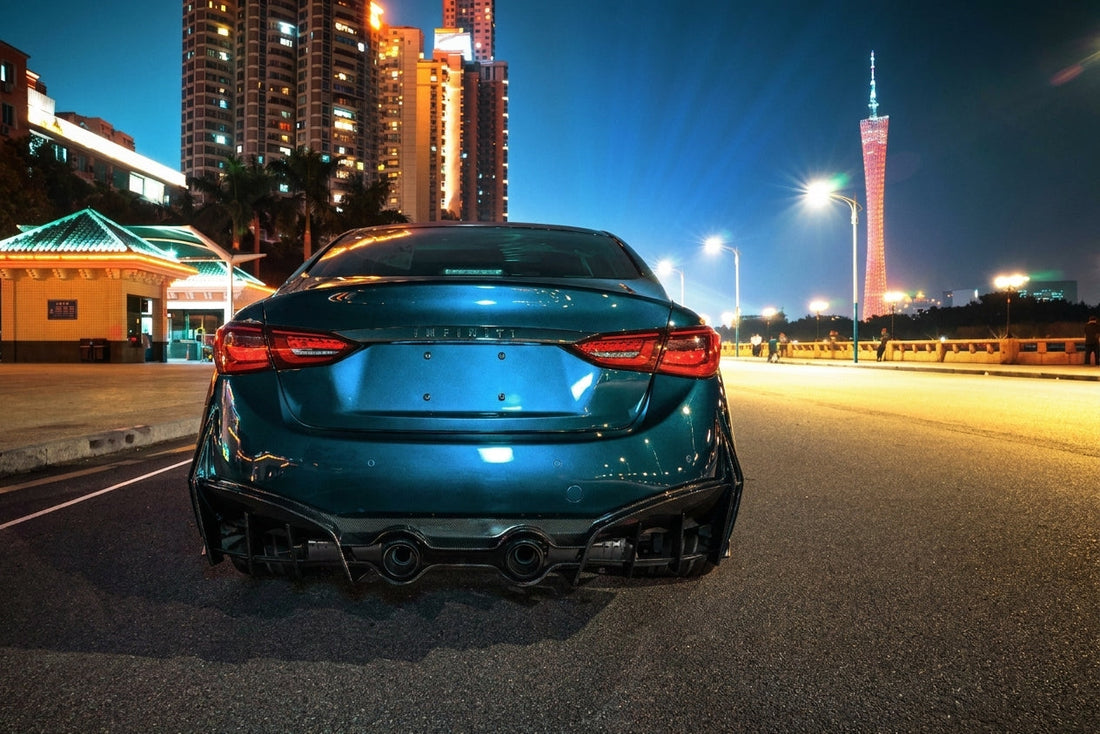 Dark teal Infiniti Q50 wearing the CMST Ultimate Edition kit with carbon front lip, Q60-style grille and carbon side skirts, front three-quarter low angle