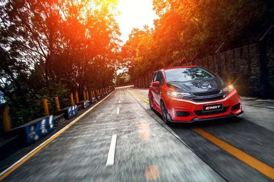 Red Honda Fit hatch wearing the CMST aero kit with carbon front lip, grille and vented carbon bonnet, front three-quarter low angle