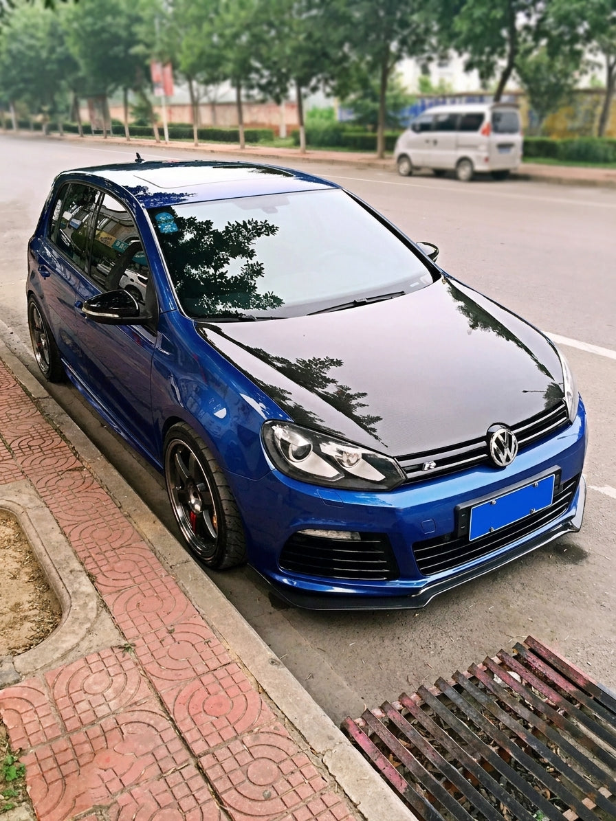 CMST Volkswagen Golf MK6 with carbon fibre R-style front lip and rear lip, 3/4 front low angle, white body, moody garage lighting, shallow depth of field, visible carbon weave, no text