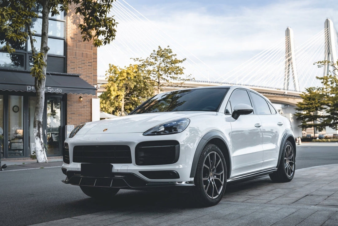 White Porsche Cayenne Coupe wearing the CMST carbon-fibre kit, front three-quarter low angle with carbon front lip, side skirts and gloss weave
