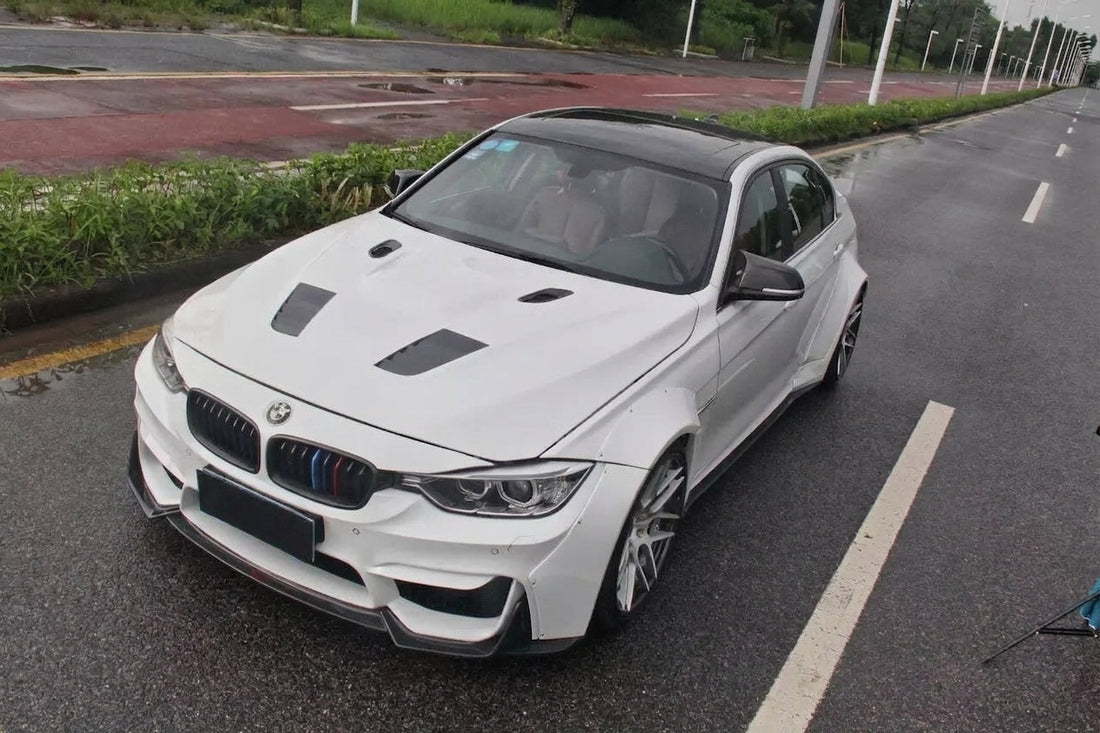 BMW 3 Series F30 in white wearing the CMST carbon widebody aero kit with M-style front, front three-quarter low angle showing carbon lip and flared arches