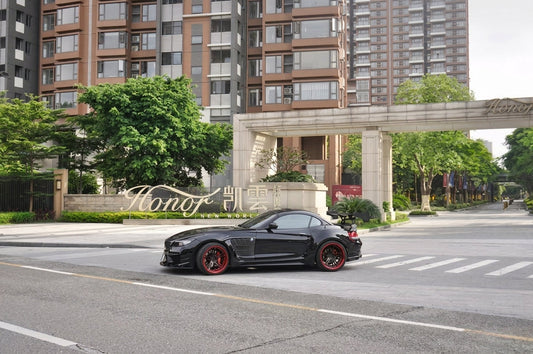Black BMW Z4 E89 roadster in the CMST widebody carbon and FRP kit on two-piece forged wheels with red barrels and dual-dual carbon exhaust tips, front three-quarter low angle