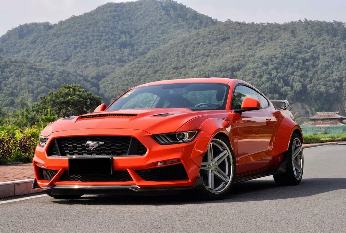Competition-orange 2015-2017 S550 Ford Mustang wearing the CMST dry-carbon widebody kit, front three-quarter low angle with visible carbon weave aero on silver 20-inch 5-spoke wheels