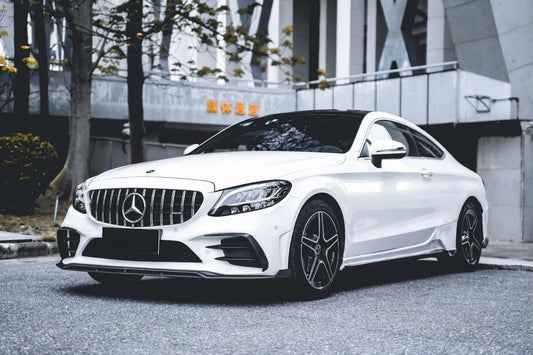 Pearl white Mercedes-Benz C-Class Coupe C205 wearing a CMST carbon fibre kit and GT grille, front three-quarter low angle in a studio