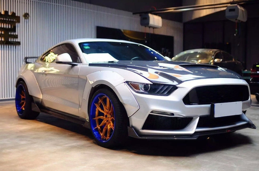 Silver 2015-2017 S550 Ford Mustang with the CMST widebody kit on 20-inch CMST CT201 2-piece forged wheels with a gold face and blue lip, red Brembo brakes behind, low front three-quarter studio angle