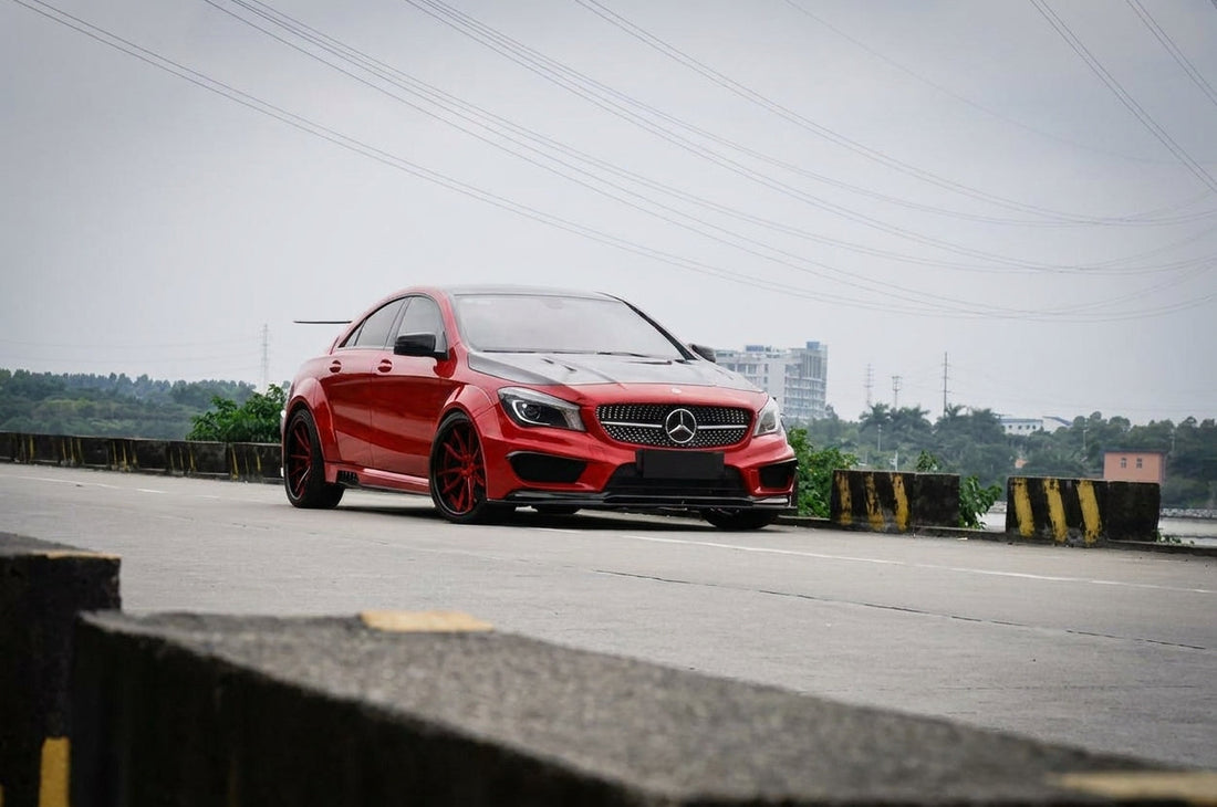 Red Mercedes-Benz CLA C118 widebody wearing a CMST carbon fibre aero kit, front three-quarter low angle in a moody studio