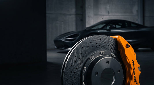 Close-up of a high-performance McLaren carbon ceramic brake rotor and orange caliper, showcasing lightweight automotive engineering for P1 and 720S models.