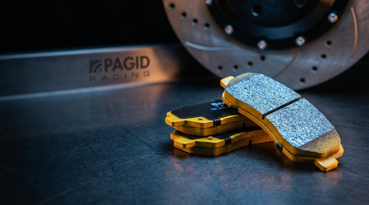 A professional comparison layout of Pagid RS29, RS14, RST3, and RSC1 racing brake pads next to a high-performance ventilated brake rotor in a racing garage.